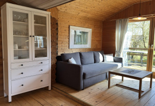 Woonkamer van houten lodge in Duitsland met grijze bank, witte kast en uitzicht op zonnig terras.
