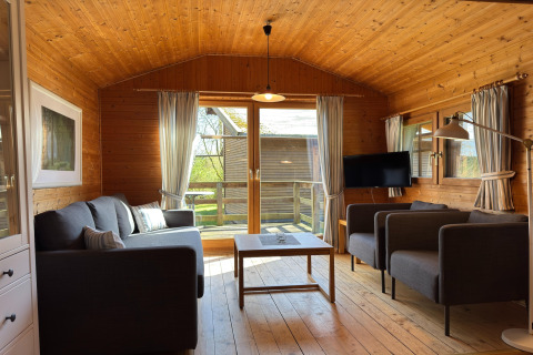Houten woonkamer in een Duits lodge met sofa’s, tv, salontafel en uitzicht op het terras.
