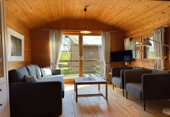 Sala de estar con paneles de madera en una casa de campo en Alemania, con sofá, TV y acceso a la terraza.
