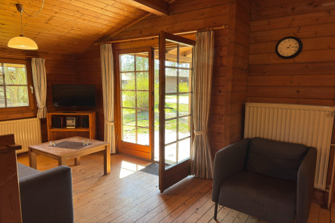 Gezellige woonkamer in houten chalet met open deur naar de tuin, zetel, bank en tv, Type C House Duitsland.
