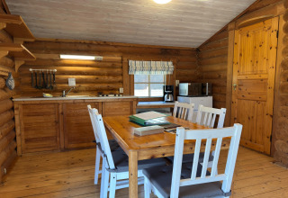 Binnenzicht van een gezellige blokhut in Duitsland met keuken, eettafel, vier witte stoelen en houten muren.