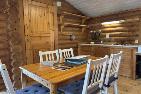 Binnenzicht van een houten lodge met eettafel, vier stoelen, open planken en kleine keuken in Duitsland.