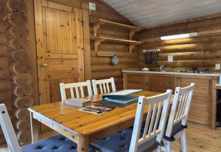 Interieur van een houten lodge met eettafel, vier stoelen, open planken en kleine keuken in Duitsland.