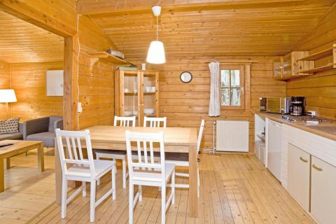 Gezellig houten lodge-interieur met eettafel, witte stoelen en keuken in Duitsland, Type C House.