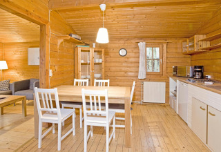 Gezellig houten lodge-interieur met eettafel, witte stoelen en keuken in Duitsland, Type C House.