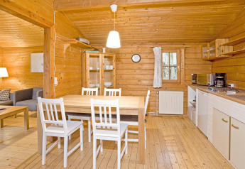 Intérieur chaleureux de lodge en bois avec table, chaises blanches et cuisine, en Allemagne, Type C House.