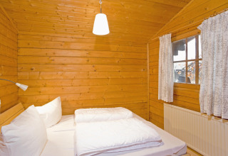 Bedroom in a wooden lodge featuring a double bed, white linens, and window in Type C House, Germany.
