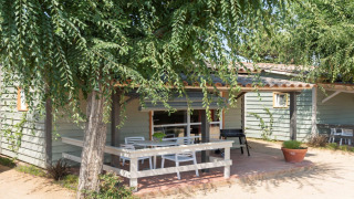 Buitenterras van Camping del Mar BUNGALOW PREMIUM met zithoek, omgeven door bomen en groen.