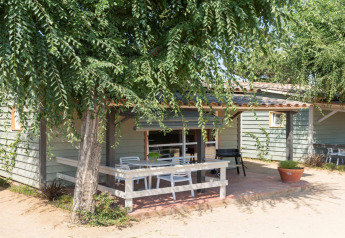 Terraza al aire libre del Camping del Mar BUNGALOW PREMIUM, con mesa y sillas bajo árboles verdes.