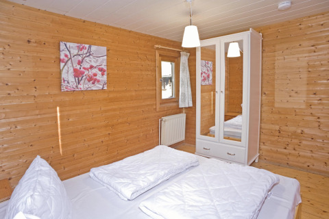 Slaapkamer in lodge ‘Type C House 363 364 361 362’ in Duitsland met houten wanden en wit beddengoed.
