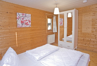 Slaapkamer in lodge ‘Type C House 363 364 361 362’ in Duitsland met houten wanden en wit beddengoed.