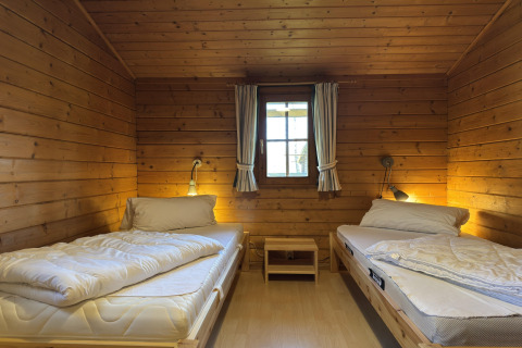 Houten kamer met twee eenpersoonsbedden, centraal raam en nachtkastjes in Type C House in Duitsland