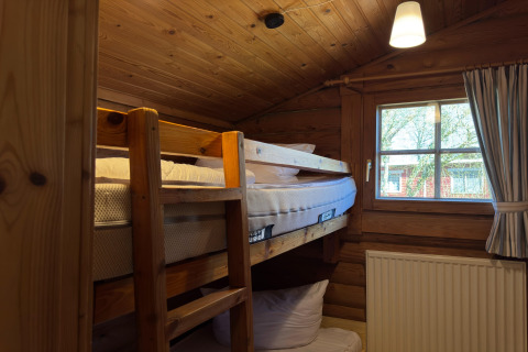 Gezellige houten lodge in Duitsland met stapelbed, raam, radiator en gordijn met houten plafond.