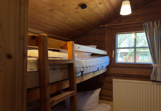 Cozy wooden lodge room in Germany with bunk bed, window, radiator, lamp, and wooden ceiling.