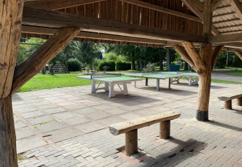 Tables de ping-pong extérieures sous un abri en bois avec des bancs, pelouse et aire de jeux en Allemagne.