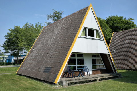Et A-formet lodgelignende hus med terrasse og havemøbler, omgivet af græs og træer i Tyskland.