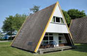 Casa estilo cabaña tipo A con terraza y muebles de jardín, rodeada de césped y árboles en Alemania.
