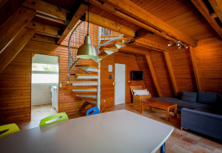 Interior of a cozy wooden lodge featuring a spiral staircase, modern living area, and open kitchen space