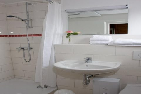 Stijlvolle badkamer met douche, witte tegels, wastafel, grote spiegel en nette handdoeken op de plank.