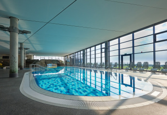 Indoor swimming pool at a modern lodge, with large windows, lounge chairs, and a view outside.