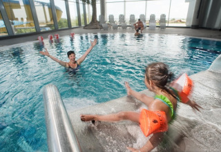 Binnenzwembad in een lodge, kind met oranje zwembandjes spettert op de treden naast een volwassene.