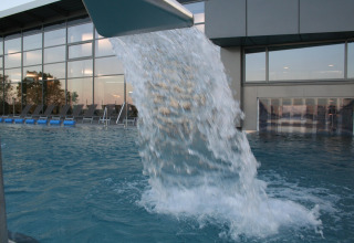 Outdoor pool at a lodge, featuring a waterfall fountain and lounge chairs, beside a modern glass building.