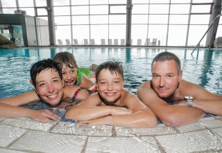 En glad familie på fire slapper af sammen i en indendørs pool på et moderne lodge med store vinduer.
