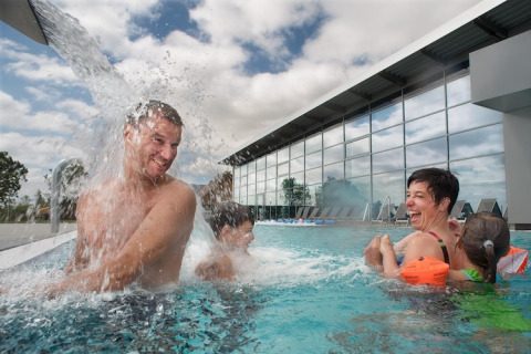 Gezin beleeft plezier in het zwembad bij een lodge, man onder waterval en kinderen met bandjes.