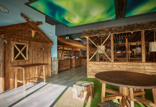 Interiør af en lodge med træmøbler, rustikt design og kunstigt nordlys på loftet i hyggelig atmosfære.