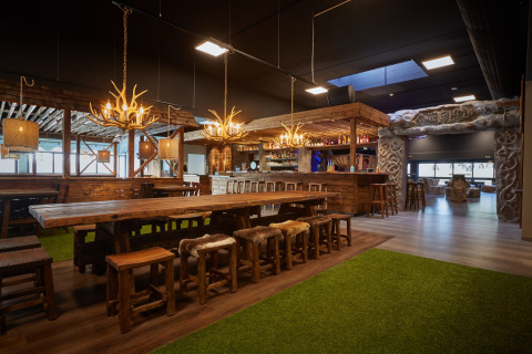 Sfeervol lodge-interieur met lange houten tafels, geweilampen en een rustieke baromgeving.