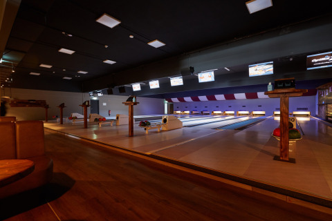 Bowling lanes inside a cozy lodge setting, featuring wooden floors, monitors, and colorful bowling balls.