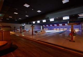 Bowlingbanen in een sfeervolle lodge met houten vloer, kleurrijke bowlingballen en schermen.