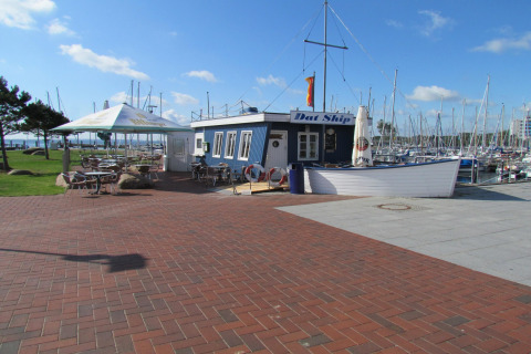 Foto van een gezellige lodge bij de jachthaven met buitenterrassen en veel zeilboten op de achtergrond.
