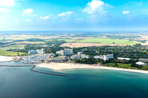 Luchtfoto van een kustplaats met jachthaven, hotels en zandstranden, omgeven door groene velden en natuur.