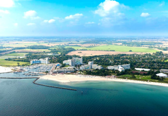 Vista aerea di una città costiera con marina, hotel, spiagge sabbiose e campi verdi che si estendono lontano.