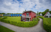 Casa a terrazza rossa a Ostseeresort Dampland, Germania, circondata da siepi e altre case colorate.