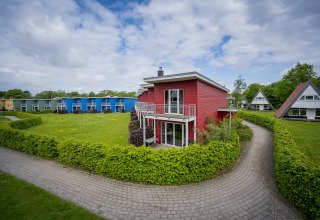 Rødt terrassehus i Ostseeresort Dampland, Tyskland, omgivet af grønne hække og farverige huse.
