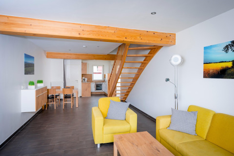 Moderne stue i Ostseeresort Dampland-Terrace house HiPr med gule sofaer, trappe og åbent køkken.