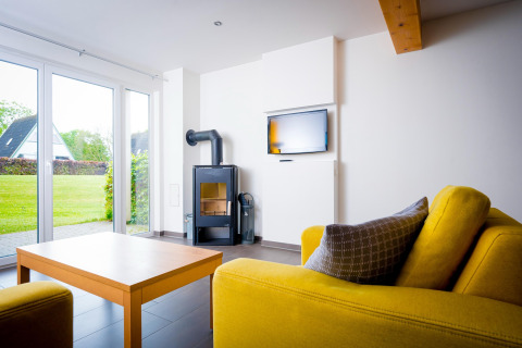 Lichte woonkamer in Ostseeresort Dampland-Terrace house HiPr, Duitsland, met gele bank en houtkachel.