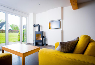 Lichte woonkamer in Ostseeresort Dampland-Terrace house HiPr, Duitsland, met gele bank en houtkachel.