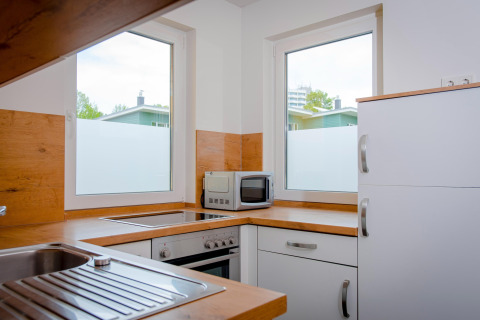Moderne køkken med hvide skabe, træbordplader, komfur og mikroovn ved Ostseeresort Dampland-Terrace house HiPr.