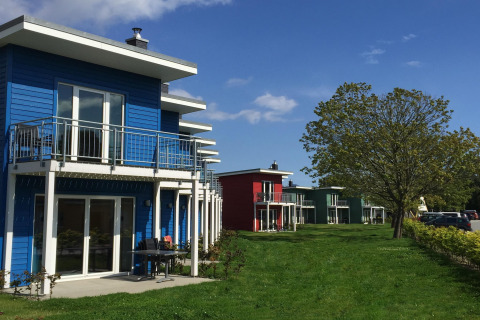 Række af farverige terrassehuse på Ostseeresort Dampland i Tyskland med grønne og blå nuancer.