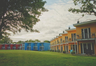 Kleurrijke terraswoningen bij Ostseeresort Dampland in Duitsland, omgeven door grasveld en bomen.