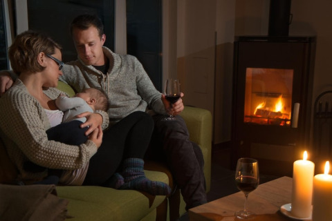 En familie hygger sig foran pejsen med levende lys og et glas vin i lodge Ostseeresort Dampland-Terrace house HiPr i Tyskland.