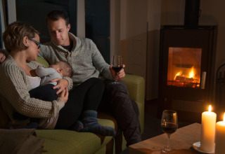 Een gezin ontspant bij de open haard met kaarsen en wijn in Ostseeresort Dampland-Terrace house HiPr in Duitsland.