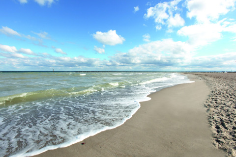 Rustig zandstrand met zachte golven en blauwe lucht, gefotografeerd vanaf een lodge aan zee.