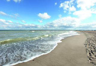 Vredig strand met lichte golven en blauwe lucht, vastgelegd vanaf een lodge aan de kust.