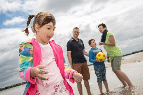 Blije familie speelt op het strand bij Ostseeresort Dampland-Terrace house HiPr, Duitsland, op een bewolkte dag.