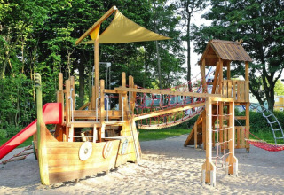 Parco giochi all'aperto con nave in legno, scivolo, ponte di corde e rete da arrampicata al lodge.