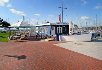 Gemütliches Café am Yachthafen mit vielen Segelbooten, blauem Haus und Schild 'Dat Ship'.